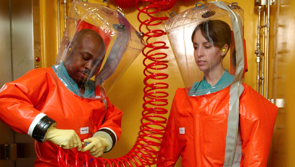 CDC scientists connect to a supportive air hose to breathe air and to maintain positive pressure inside the protective, BSL4 lab suit. Photo Credit James Gathany, Centers for Disease Control and Prevention.